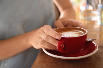 Woman with cup of fresh aromatic coffee at table, closeup