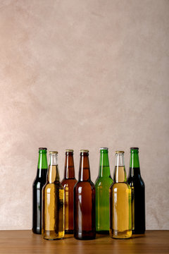 Bottles with different beer on table against color background