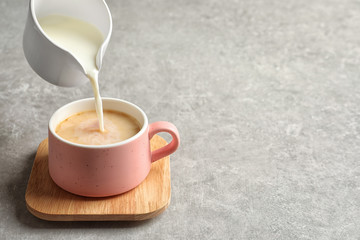 Pouring milk into cup of black tea on gray table