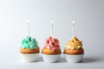 Delicious birthday cupcakes with candles on gray background