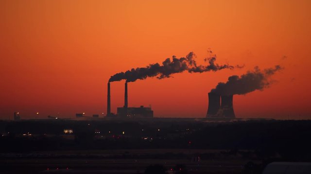 Air Pollution from Power Plant on the Horizon of a Vibrant Orange Dawn releasing Smoke into the Sky