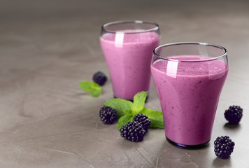 Glasses with blackberry yogurt smoothies on grey table