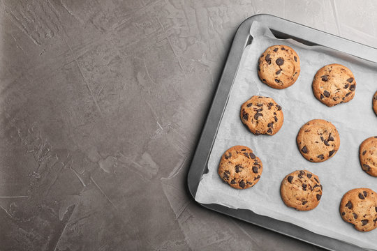 Baking sheet with chocolate chip cookies and space for text on grey background, top view