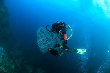 SCUBA divers attempting to remove a huge ghost fishing net tangled over a large area of a tropical...