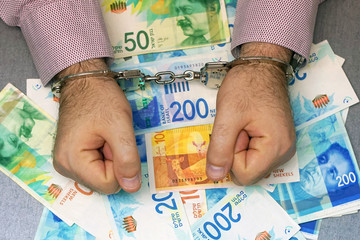 Businessman in office in handcuffs holding a bribe of Israeli money. Close-up hands in handcuffs. Arrested terrorist. Financial crime, dirty money and corruption concept. Selective focus.