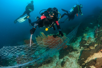 SCUBA divers attempting to remove a huge ghost fishing net tangled over a large area of a tropical coral reef