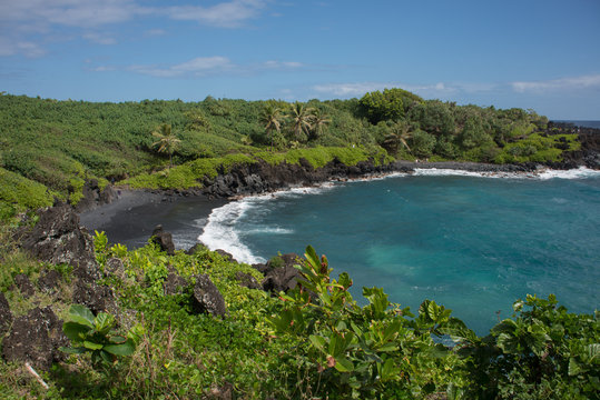 Looking down to the Waianapanapa Black Sand Beach on the island of Maui, Hawaii surrounded by lush foliage.
