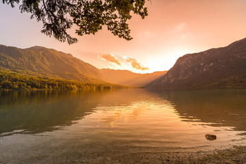 Obraz premium Sunset above the Bohinj lake, Slovenia. Magical evening color of sun with reflection in water. Julian Alps in background. Triglav national park