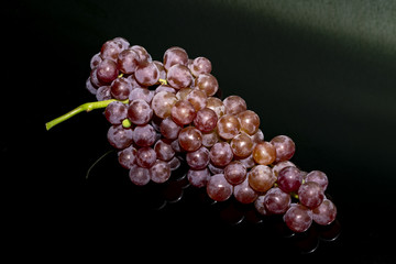 a bunch of pink grapes lies on a black glass table