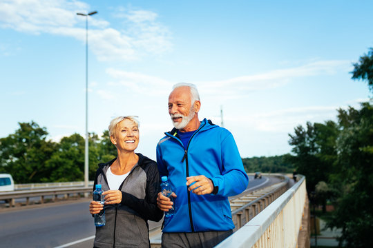 Happy fit senior couple jogging along city bridge.