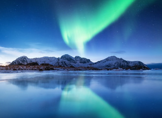Fototapeta na wymiar Aurora borealis on the Lofoten islands, Norway. Green northern lights above mountains. Night sky with polar lights. Night winter landscape with aurora and reflection on the water surface.