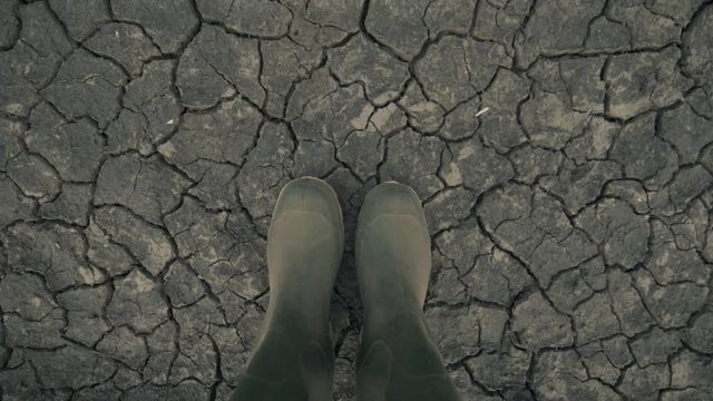 Farmer in rubber boots standing on dry soil ground, global warming and climate change is impacting crops growing and yield