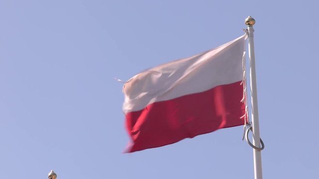 Polish flag on the mast. The wind blows hard. White and red colors. Polish emblem.  Shallow depth of fields.	