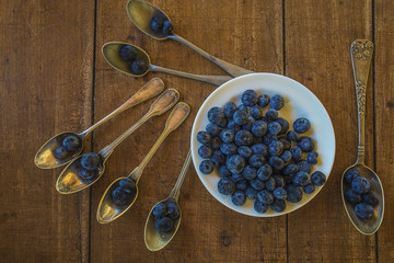 White plate and little vintage spoons wity blackberries top view on old wooden background