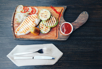 Grilled chicken fillet with vegetables and sauce on a wooden board. top view