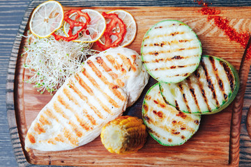 Grilled chicken fillet with vegetables and sauce on a wooden board. top view