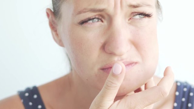 The woman holds her hand to her cheek. She removes her hand from the sore spot. One cheek swollen. Inflammation after implant placement, swelling and pain
