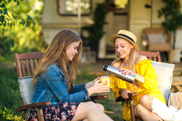 Girls with a thermos in armchairs by the fire outside the city. Pleasure to spend time with people close to nature