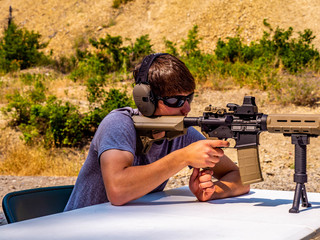 A young man concentrates as he fires his rifle at a paper target down range.
