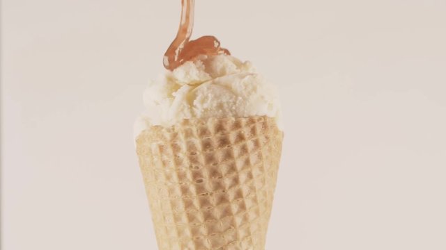 Pouring berry jam over ice cream cone, close-up shot