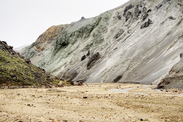 Fototapeta premium Pale Gray-Green Rhyolite Ridge with Dark Erosion Gullies Above a Sandy Valley in the Rainbow Mountains, Iceland