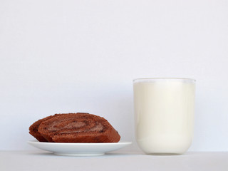 Sweet breakfast: a glass of milk and a few slices of chocolate roll on a saucer on a light background close-up