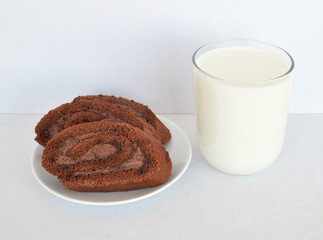 Sweet breakfast: a glass of milk and a few slices of chocolate roll on a saucer on a light background close-up