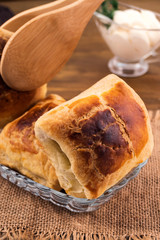 Oven-cooked puff pastry bun with brown crust, kitchen tongs, linen napkin, sour cream gravy boat, close-up, vertical frame, wooden background.