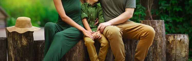 happy family of tourists parents hugging their son and sitting on wooden beams in a picturesque place near lies a woman's hat