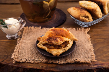 Sweet dessert of puff pastry with Apple filling, sour cream sauce and herbal tea, all on wooden background.