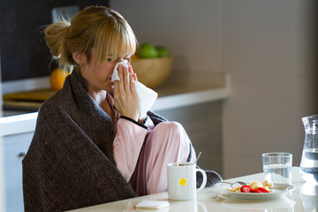 Illness young woman sneezing in a tissue at home.