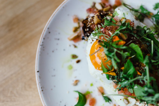 Avocado Toast with a Fried Egg Bacon Arugula Sunflower Seeds and Fresh Salsa on a Simple White Plate and Bamboo Table