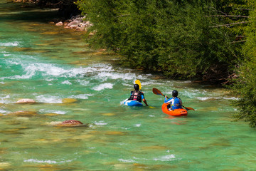 A couple kayaking in emerald, turquoise mountain river, approaching rapids in front of them