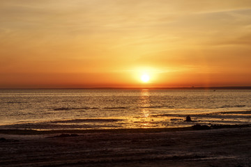 Beautiful sunset over the sea. The sun sets on the water. The sky is painted with golden bright colors. Summer evening. Sunset beach.