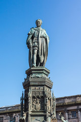 Fototapeta na wymiar Edinburgh, Scotland, UK - June 13, 2012; Statue of Walter Montagu Douglas Scott, Duke of Buccleuch on Parliament Square against blue sky. Greenish bronze of man looking down on us. Deer images.
