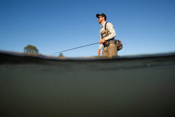 Over underwater shot of a man fly fishing in the summer in a river