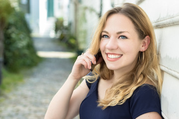 Portrait of a young woman blonde with blue eyes speaking on a mobile outdoors, smiing.