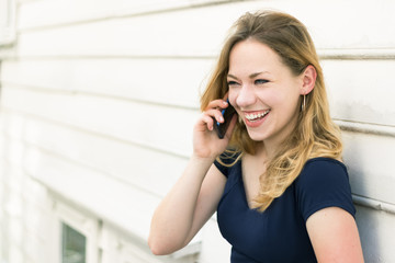 Portrait of a young woman blonde with blue eyes speaking on a mobile outdoors, laughing.
