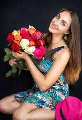 Happy, beautiful woman sitting with a bouquet of roses, on a black background. A gift for woman.
