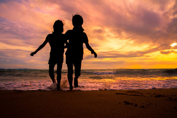 Silhouette children group enjoy playing sea waves on the beach in sunset with beautiful twilight sky