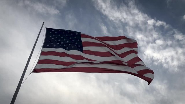 The flag of the United States of America flying against a cloudy sky at twilight.