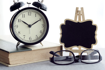 Books, alarm clock, spectacles and a black board over white curtain background