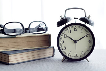 An alarm clock, spectacles and books over white curtain background