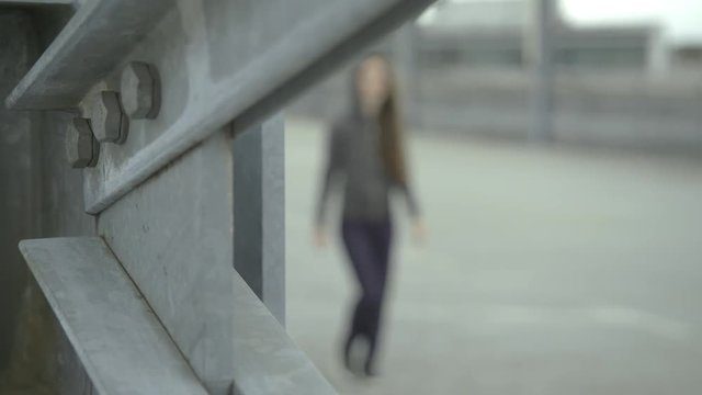 Hip hop girl with a hoody walks very cool by. Focus is set on concrete elements in front