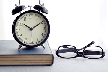 An alarm clock, spectacles and books over white curtain background
