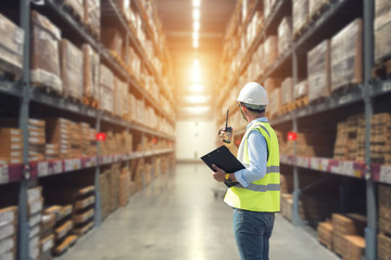 Warehouse worker talking on the phone holding clipboard in a large warehouse,logistics concept.