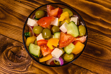 Glass bowl with greek salad on wooden table. Top view