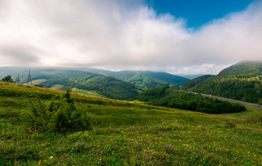 low clouds above the mountainous countryside. power line tower and roadway in the distance.