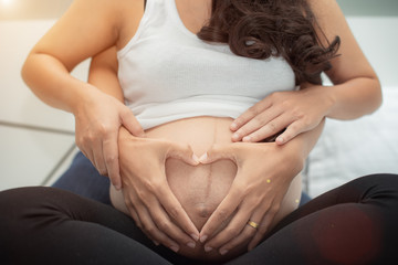 hands of husband father create gesture symbol of heart on young woman pregnant new mom, loves...
