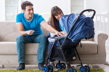 Young parents with their newborn baby in baby pram sitting on the sofa 